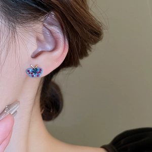 Close-up of a blue butterfly stud earring with red accents on a model's ear
