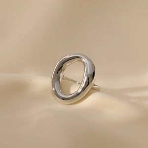 Bague ouverte argentée irrégulière et ovale évidée sur un tissu en soie beige