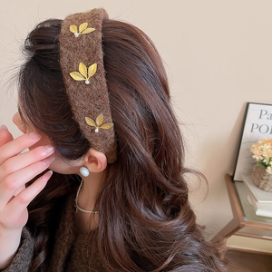 Detail of brown velvet headband with golden leaves and pearls worn by a model in soft light