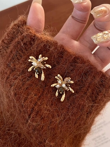 Dettaglio di orecchini floreali dorati con perle e occhio di tigre su maglione