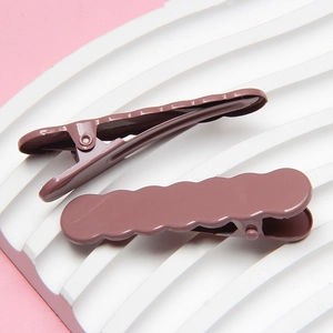 Detail of two dusty purple wavy metal hair clips on a white textured display tray