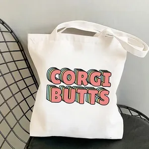 White canvas tote bag featuring retro Corgi Butts colorful graphic print on a chair