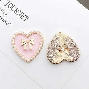 Pink enamel heart charm with pearl and bow detail next to its golden textured back
