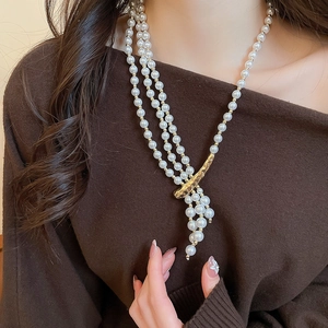 Detail of layered pearl necklace with gold hammered metal charm on brown sweater