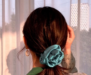 Detail of teal satin scrunchie worn on hair with elegant sunset city view backdrop