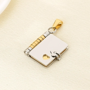 Detail of gold and silver book-shaped pendant with heart cutout on beige fabric
