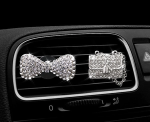 Close-up of sparkling diamond-studded bow and handbag car vent clips on air outlet