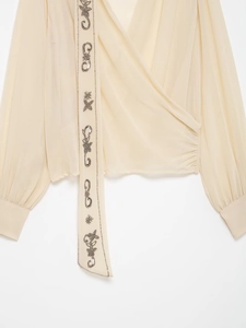 Detail of beige georgette wrap blouse with floral sequin embroidery and v-neckline