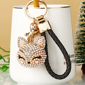 Detail of diamond fox keychain with pearls and black leather strap on a white cup