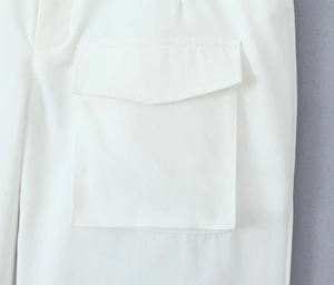 Detailed close-up of tactical cargo pockets on white twill fabric trousers with stitching