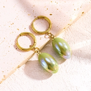 Gold hoop earrings with light green pearlescent oval resin charms on natural stone surface