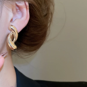 Close-up of a gold-plated twisted geometric knot stud earring worn by a model