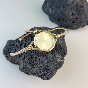 Detail of gold bracelet watch with rhinestone markers on a black volcanic rock display