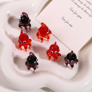 Close-up of handmade glass octopus and crab pendants in red and black on a white ceramic tray
