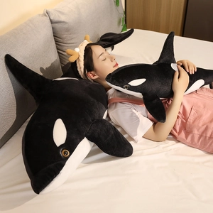 Cozy scene showing a model hugging soft black and white plush orca toys in bed