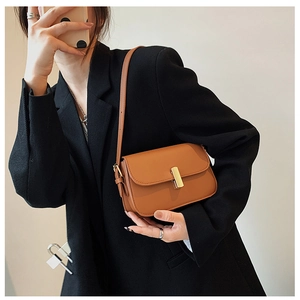 Brown leather rectangular crossbody bag with a gold lock worn over a black blazer jacket