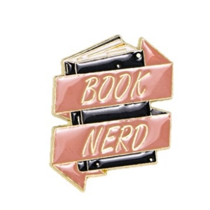 Cartoon enamel book brooch with pink banners reading BOOK NERD on white background