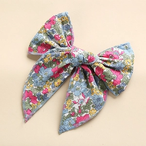 Close-up of floral cotton bow hair clip with pink and yellow flowers on blue fabric