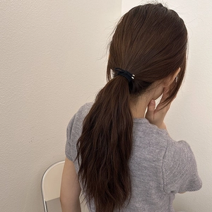 Gros plan d'un élastique à cheveux noir avec nœud métallique sur une queue de cheval