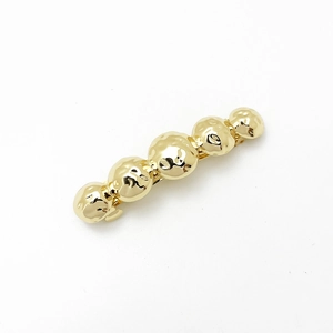 Detail of a golden metal hair clip with a beaded design and hammered texture finish