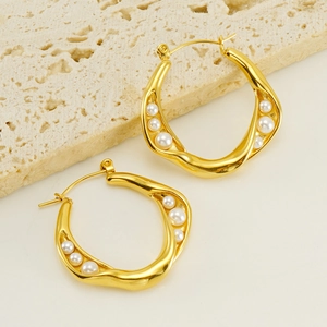 Macro shot of gold irregular hoop earrings with white pearls on a warm textured stone surface