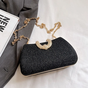 Sparkly black evening bag with gold chain strap and crystal buckle on draped fabric