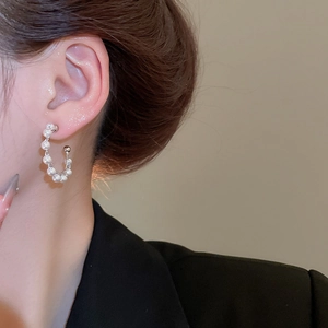 Close-up of elegant C-shaped silver hoop earrings with white pearls on a female model