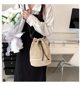 Chic beige straw bucket bag with black drawstrings shown in a lifestyle indoor setting