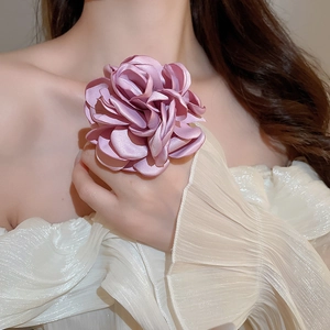 Detail eines eleganten lila Seidenblumenrings am Model mit weißem Plissee-Oberteil