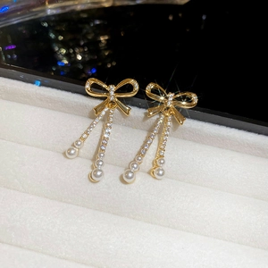 Detailed view of gold-plated bow earrings with sparkling zircons and hanging pearls