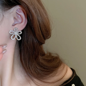 Close-up of sparkling flower-shaped stud earrings with zircons worn by a model