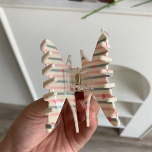 Close-up of butterfly hair claw clip with pink heart patterns and cream acrylic finish