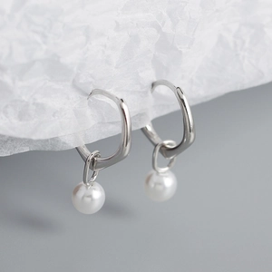 Macro detail of S925 silver geometric hoop earrings featuring elegant white pearls