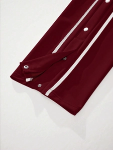 Close-up of wine red track pants with white side stripes and functional metal snap buttons