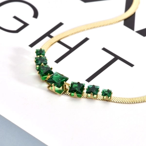 Detail of gold snake chain necklace featuring emerald green square gemstones