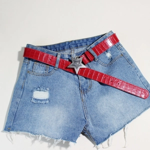 Detail eines roten Gürtels in Krokodilleder-Optik mit silberner Sternschnalle auf Denim