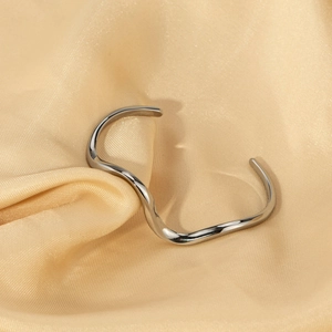 Detailed close-up of a silver wavy S-shaped open bangle on champagne gold silk fabric