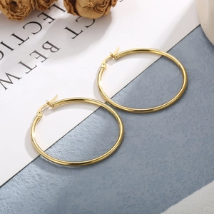Vista macro di orecchini a cerchio cavi placcati oro 18 carati su espositore in pietra