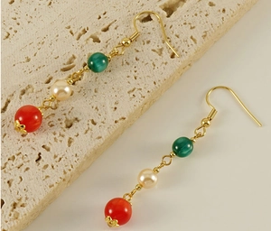 Detailed close-up of 18k gold earrings featuring green, pearl, and red agate beads