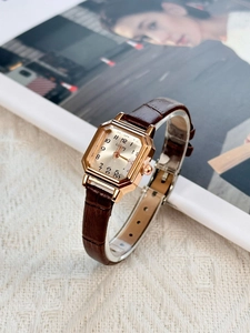 Detail view of square rose gold watch with brown leather strap on a soft fabric background