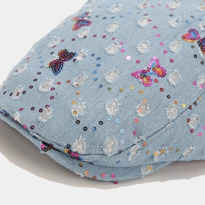 Detail view of light blue denim hat featuring colorful sequin butterfly and glitter accents