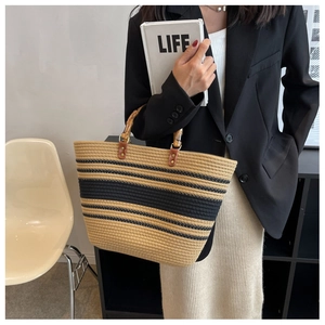 Detail of woven tote bag featuring natural bamboo handles and black striped pattern