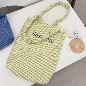 Detail of yellow checkered canvas tote bag featuring ruffled straps and black letter print