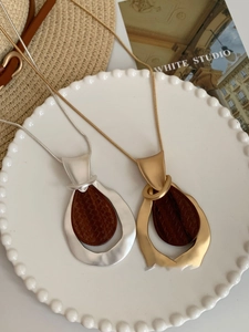 Detail of drop-shaped gold and silver necklaces with wood inlay on a white plate
