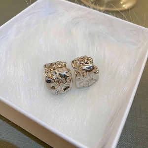 Irregular silver C-shape earrings with textured metal finish on white feathers in a gift box