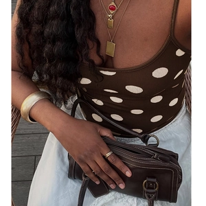 Dettaglio di crop top marrone a pois con borsa in pelle e accessori dorati alla moda