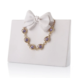 Elegant gold chain bracelet with purple heart gemstones on a white bow display stand