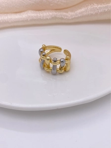 Close-up of two-tone braided open ring in gold and silver finish on a ceramic plate