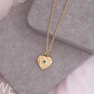 Golden heart necklace with textured finish and blue gemstone on a grey stone surface