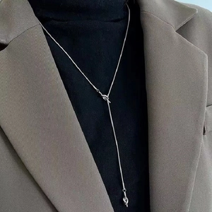 Detail of silver OT buckle Y-shaped knot necklace worn over a black turtleneck sweater